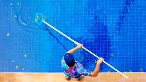 How often to use robotic pool cleaner – A person using a skimmer to clean a pool